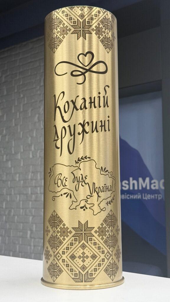 Лаконічне і ніжне оформлення: великий напис «Коханій дружині», пиксельний орнамент вишиванки зверху і знизу, посередині — контурна карта України з написом «Все буде Україна!» у каліграфічному стилі.