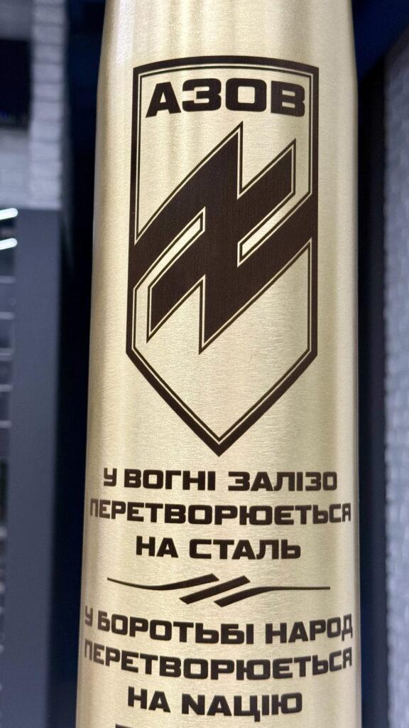 Фрагмент гільзи з шевроном АЗОВ і двома рядками девізу. Контраст і чіткість тексту на полірованій латуні демонструють точність лазерного обладнання Gravirovka.ua.