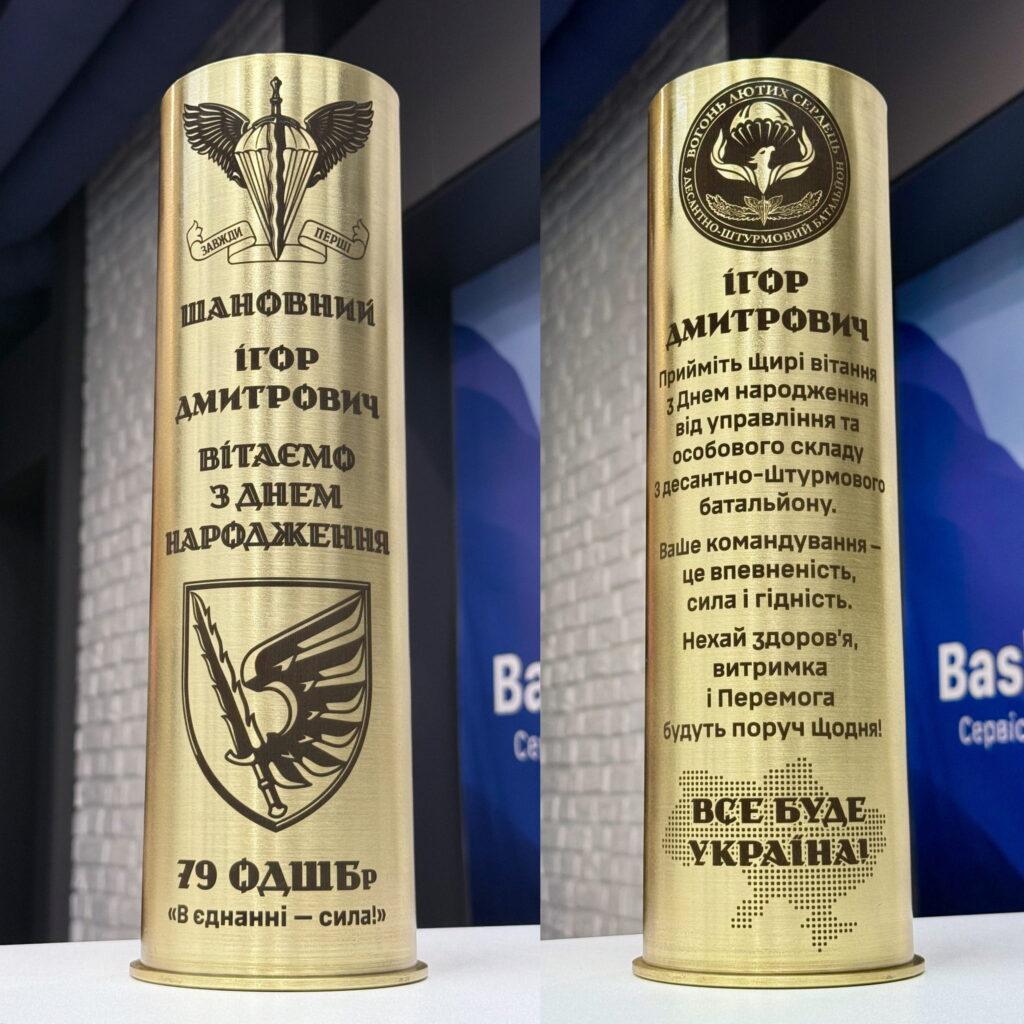 Дві сторони артилерійської гільзи — шеврон 79 ОДШБр «Завжди перші» із привітанням «Вітаємо з Днем народження» та зворотна сторона з шевроном десантно-штурмового батальйону і розгорнутими побажаннями «Все буде Україна!» Класичний двосторонній формат: лицьова сторона — ім'я та офіційне вітання, зворотна — розгорнуті щирі побажання від управління та особового складу. «Ваше командування — це впевненість, сила і гідність».